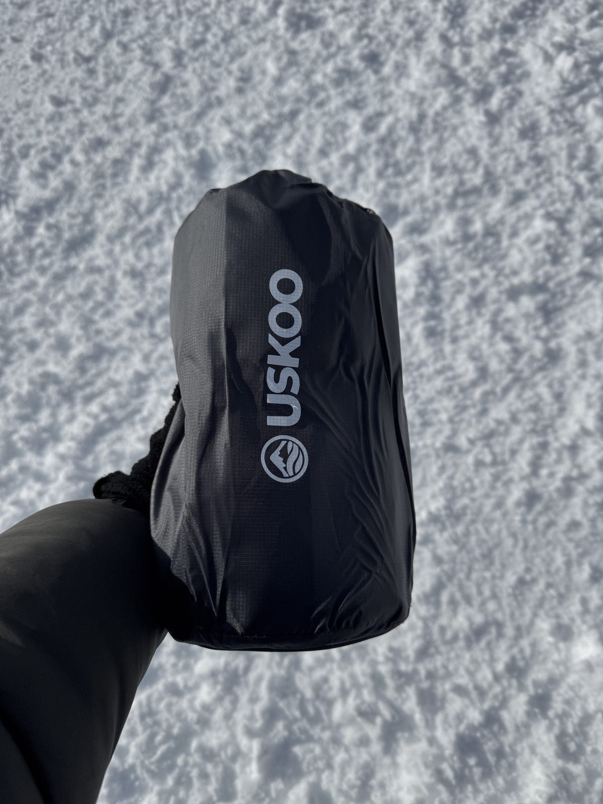 An Uskoo AirFlex packed in its compression sack, held in one hand above the snow.