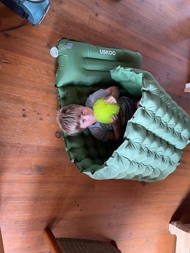 Customer photo: child curled up in a green Uskoo AirFlex pad folded into a nest