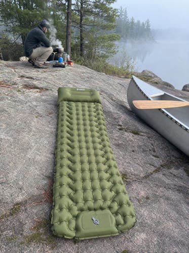 Customer photo: green Uskoo AirFlex pad on a rock slab beside a canoe at a lake