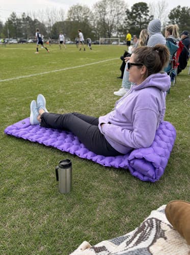 Customer photo: parent sitting on a purple Uskoo AirFlex pad on the sideline of a soccer field