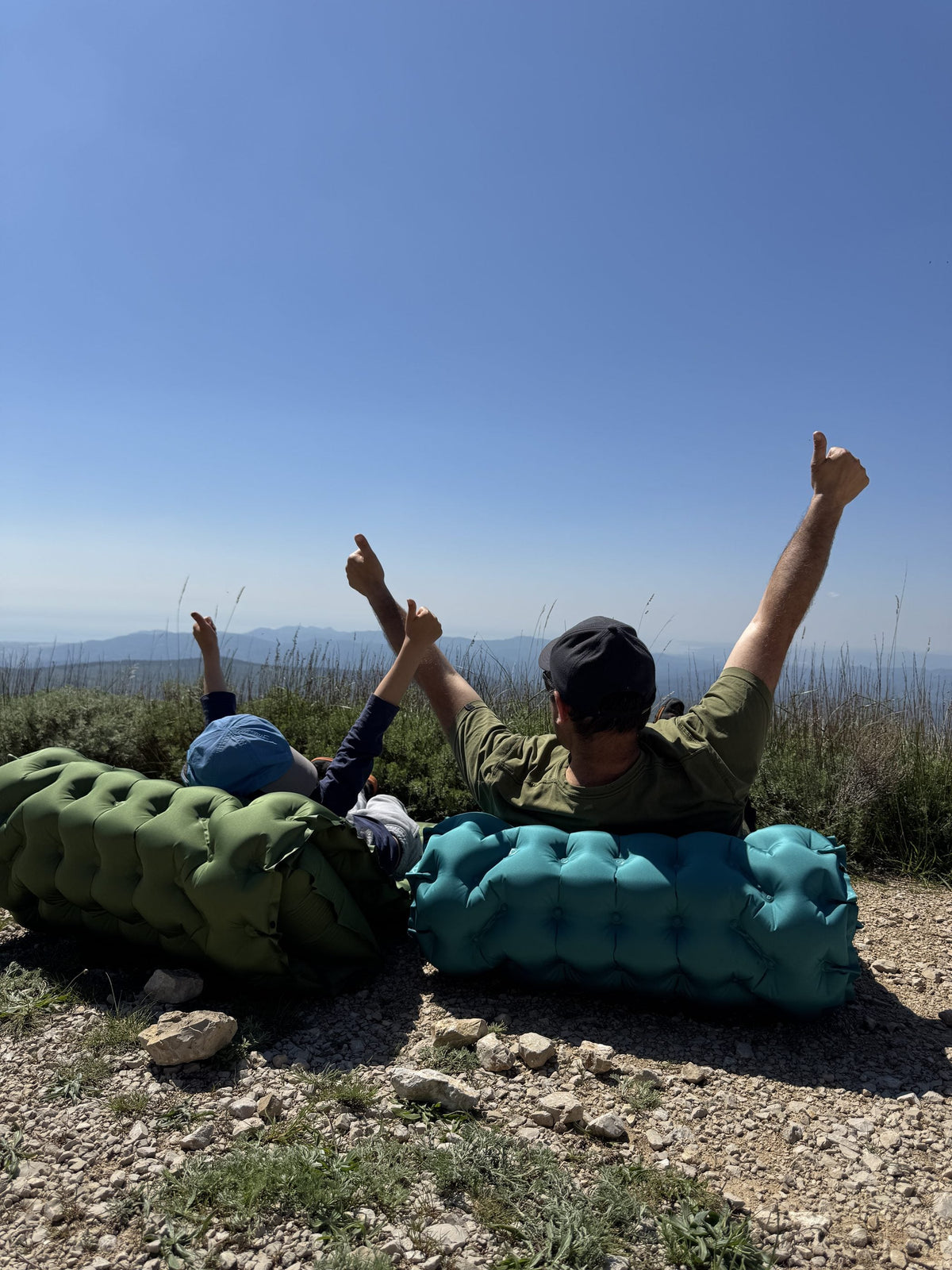 Two campers throwing their arms up on AirFlex pads above a mountain valley